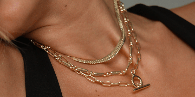 A person wearing three layered gold necklaces.