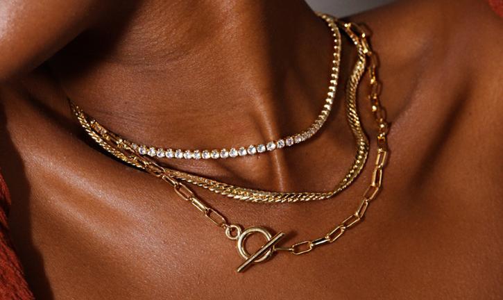 Close-up of a person's neck adorned with three gold necklaces.