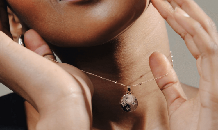 Close-up of a person with dark skin wearing a delicate gold necklace with a circular pendant.