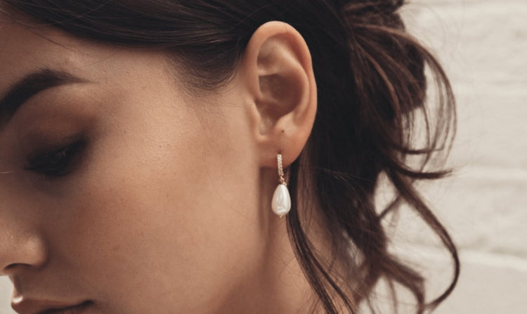 Close-up of a woman's ear wearing a pearl drop earring.