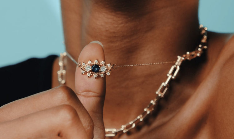 Close-up of a person holding a gold "evil eye" pendant necklace.
