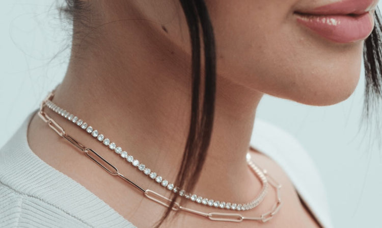 A person is wearing two necklaces: a strand of gems and a chain link necklace.
