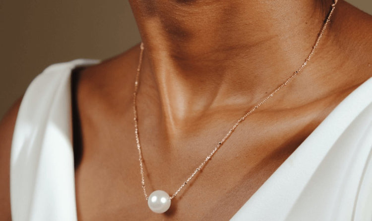 Person wearing a delicate gold chain necklace with a large white pearl pendant.