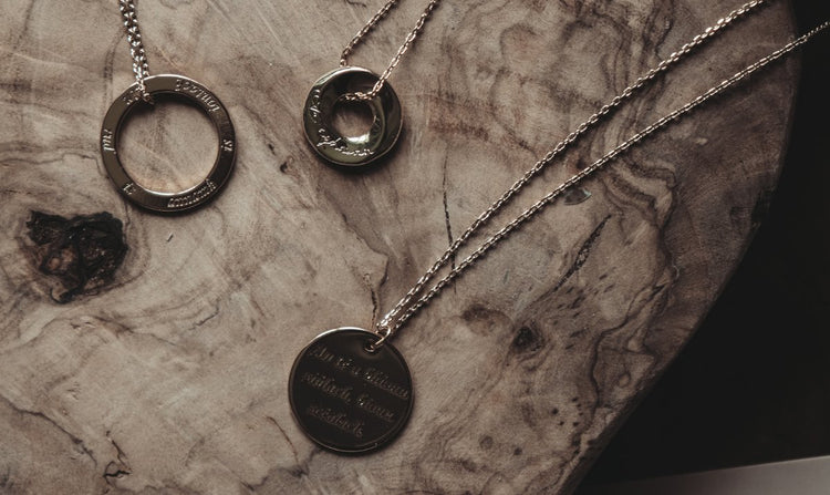 Three gold-colored pendant necklaces with engravings on a textured wooden surface.