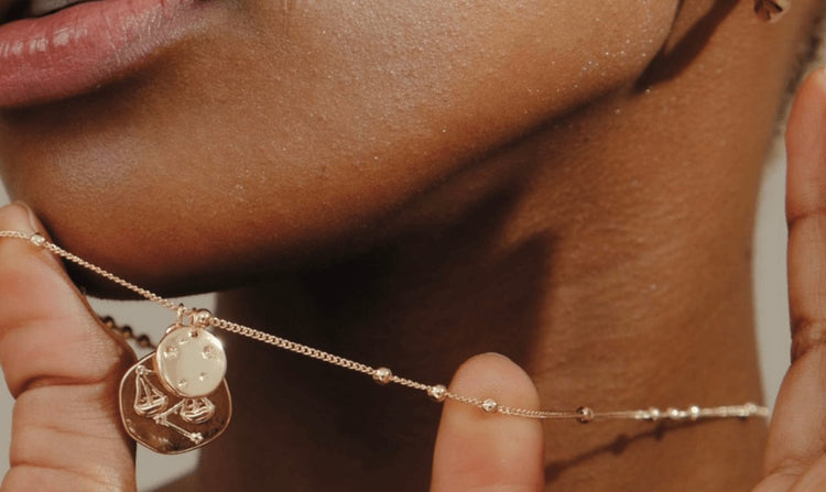 A person wearing a gold necklace with astrological charms.