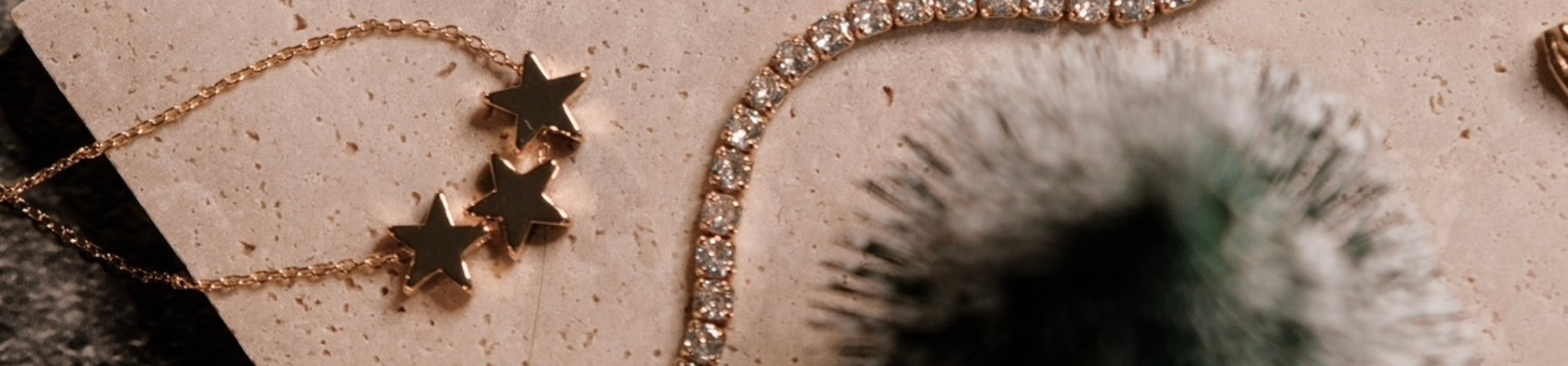 Close-up of gold star charm bracelet and a diamond tennis bracelet on a textured surface.