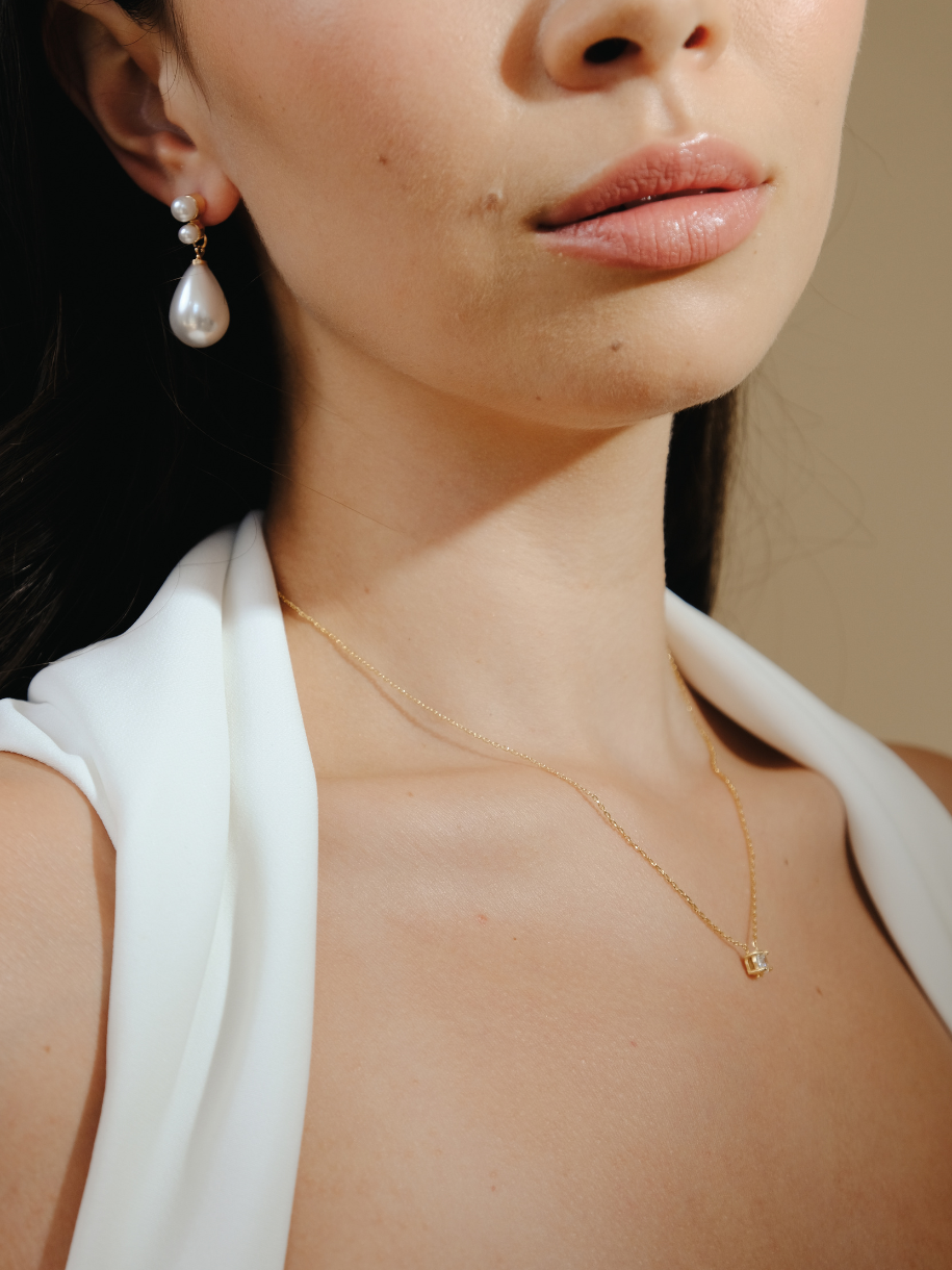Close-up of a woman wearing pearl earrings and a gold necklace with a Bridal Floating Diamante Necklace square pendant.