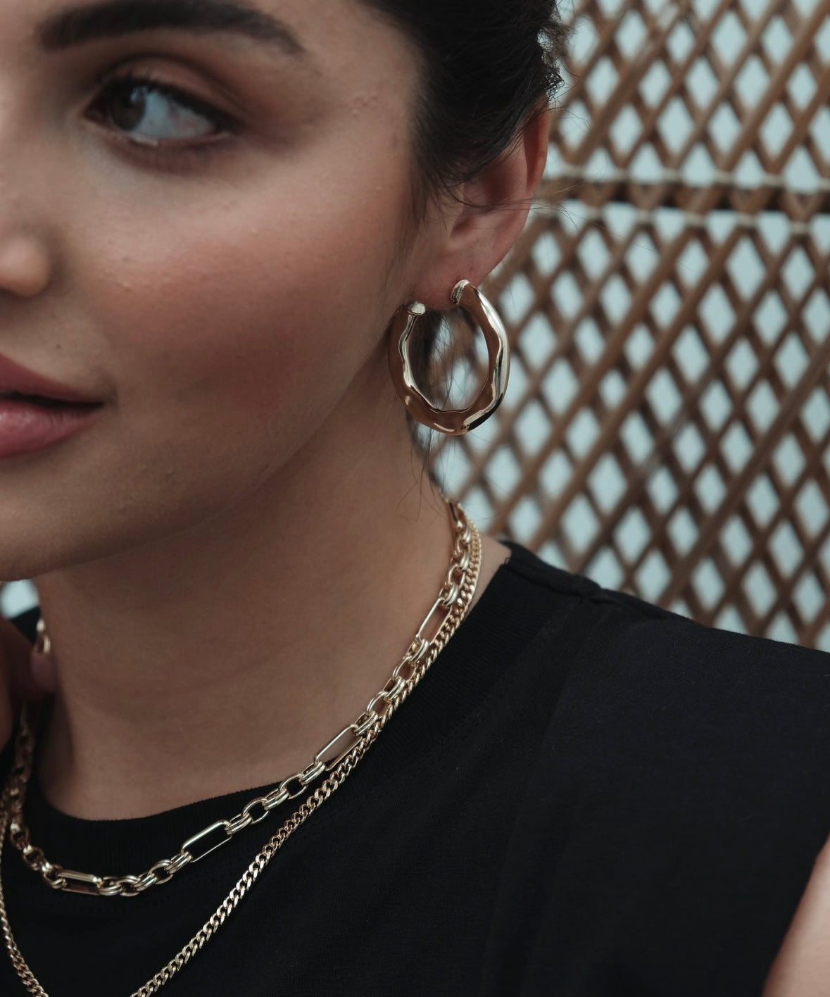Close-up of a woman with Axis Hoop earrings and layered gold necklaces.