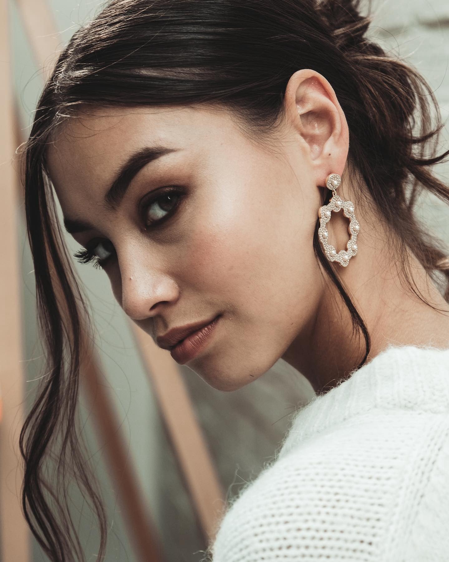 Close-up of a woman with dark hair and a white sweater wearing a Cream Crystal Hoop Earring.