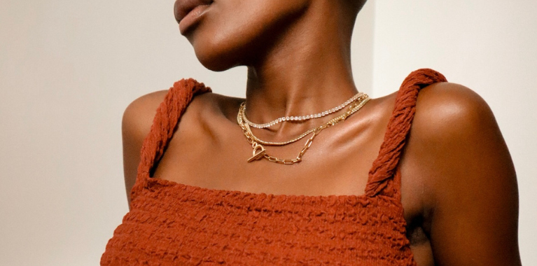 Close-up of a woman wearing a rust-colored top and layered gold necklaces.