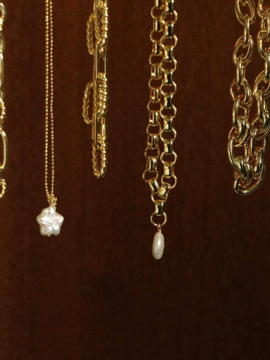 Several gold Oval Pearl Necklaces hang against a brown background, some with pearl pendants.