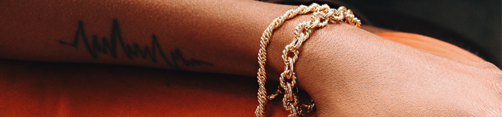 A person's forearm with a tattoo and gold bracelets.