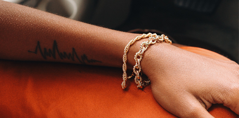 Person's arm with heartbeat tattoo and gold bracelets.