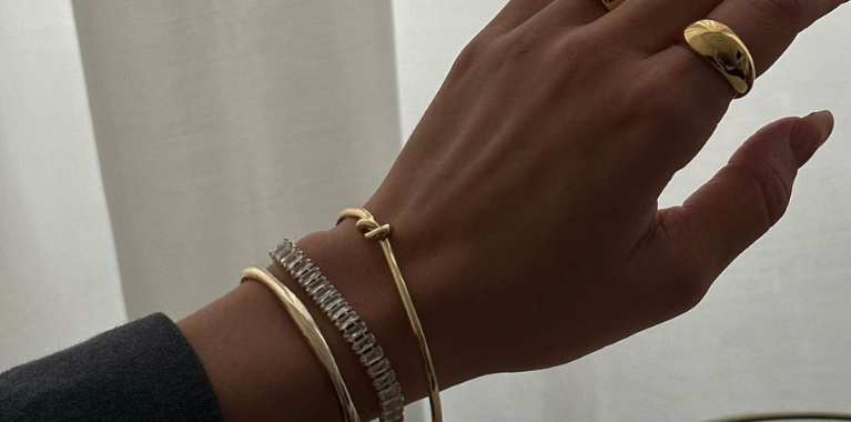 A hand displays three bracelets and a ring.