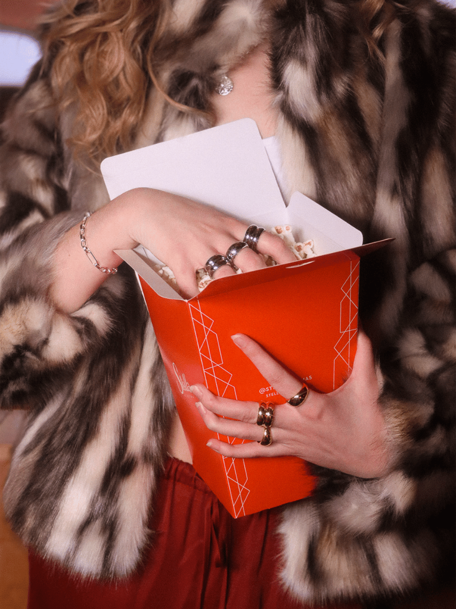 A person in a fur coat holds a red box of popcorn next to a Silver Double Dome Ring.