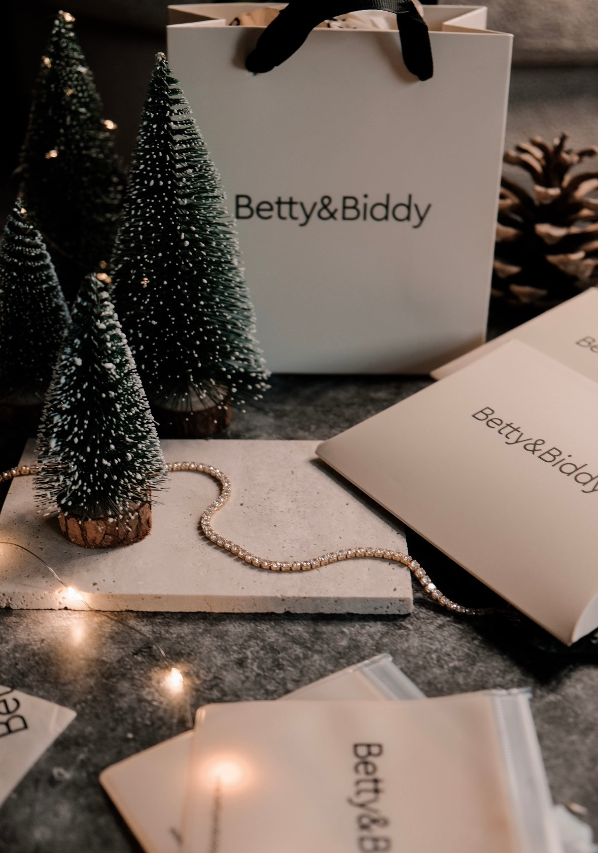 Gift Wrapping gift bag and envelopes are displayed with miniature Christmas trees, a pinecone, and a tennis bracelet.