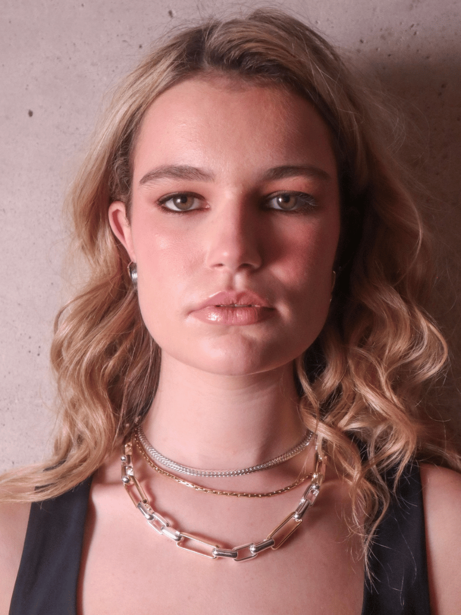 Close-up of a woman with wavy blonde hair, wearing layered necklaces including a Silver Snake Chain.