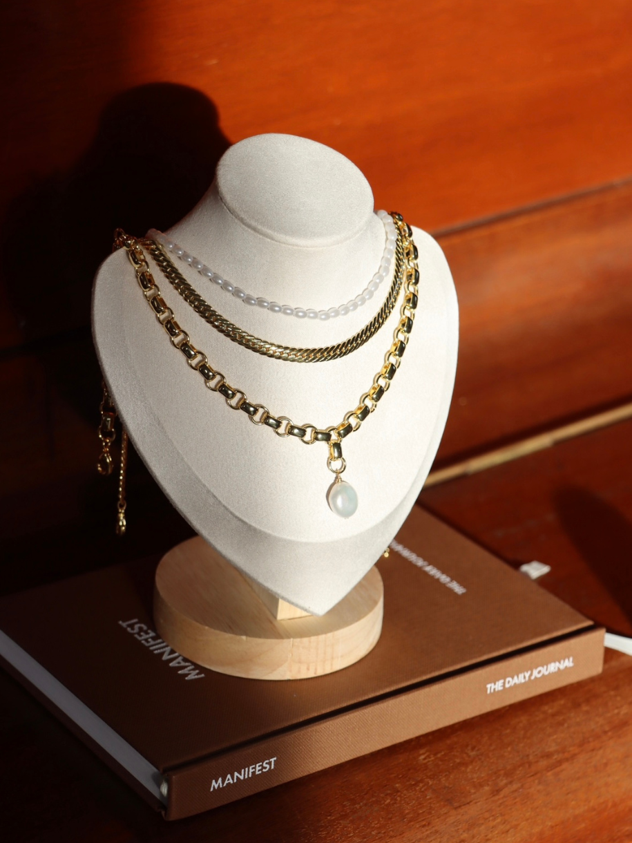 Oval Pearl Necklace displayed on a mannequin bust, which sits atop two stacked journals.