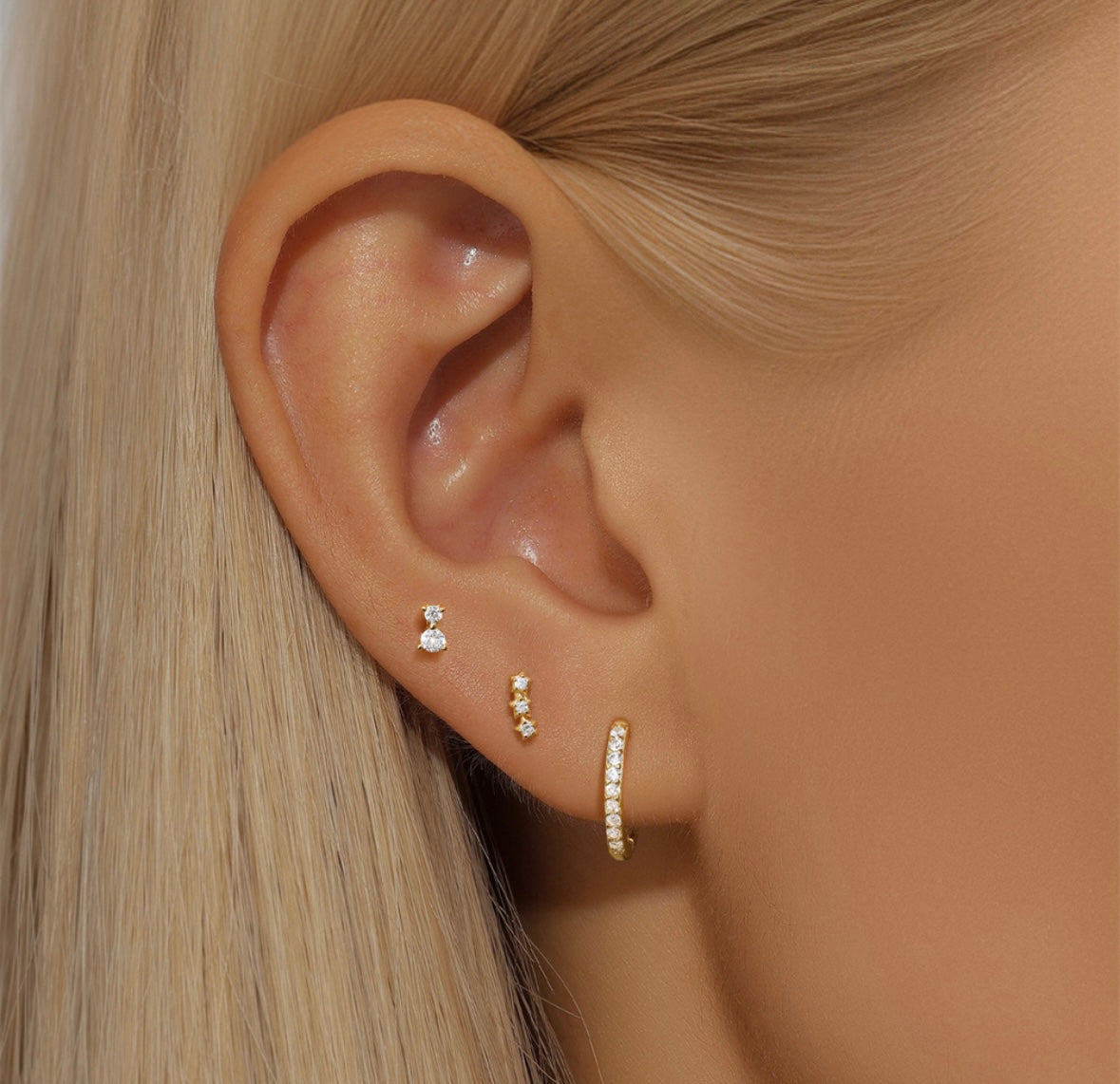 A woman's ear with three gold and gem Trio Set: Cowper Stud Set Gold earrings is seen up close.
