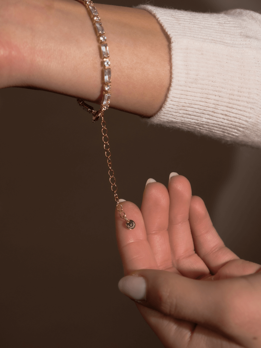 A Clear Crystal Bracelet, rose gold with baguette and round stones, is fastened around a wrist.