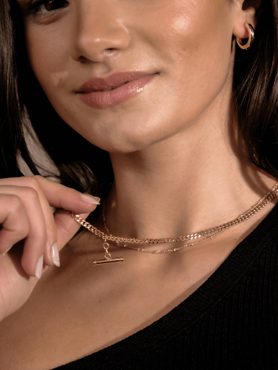 A woman wears a T-Bar Curb Chain layered gold chain necklace with a T-bar pendant.