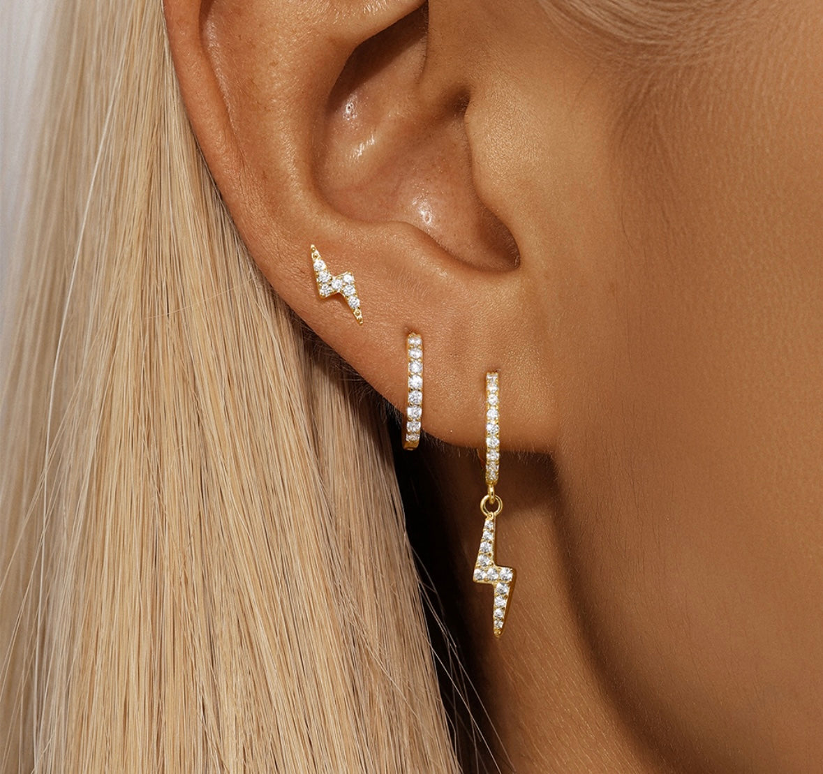 A close-up of a woman's ear with three gold and crystal Trio Set: Triple Set Bolt Gold earrings.