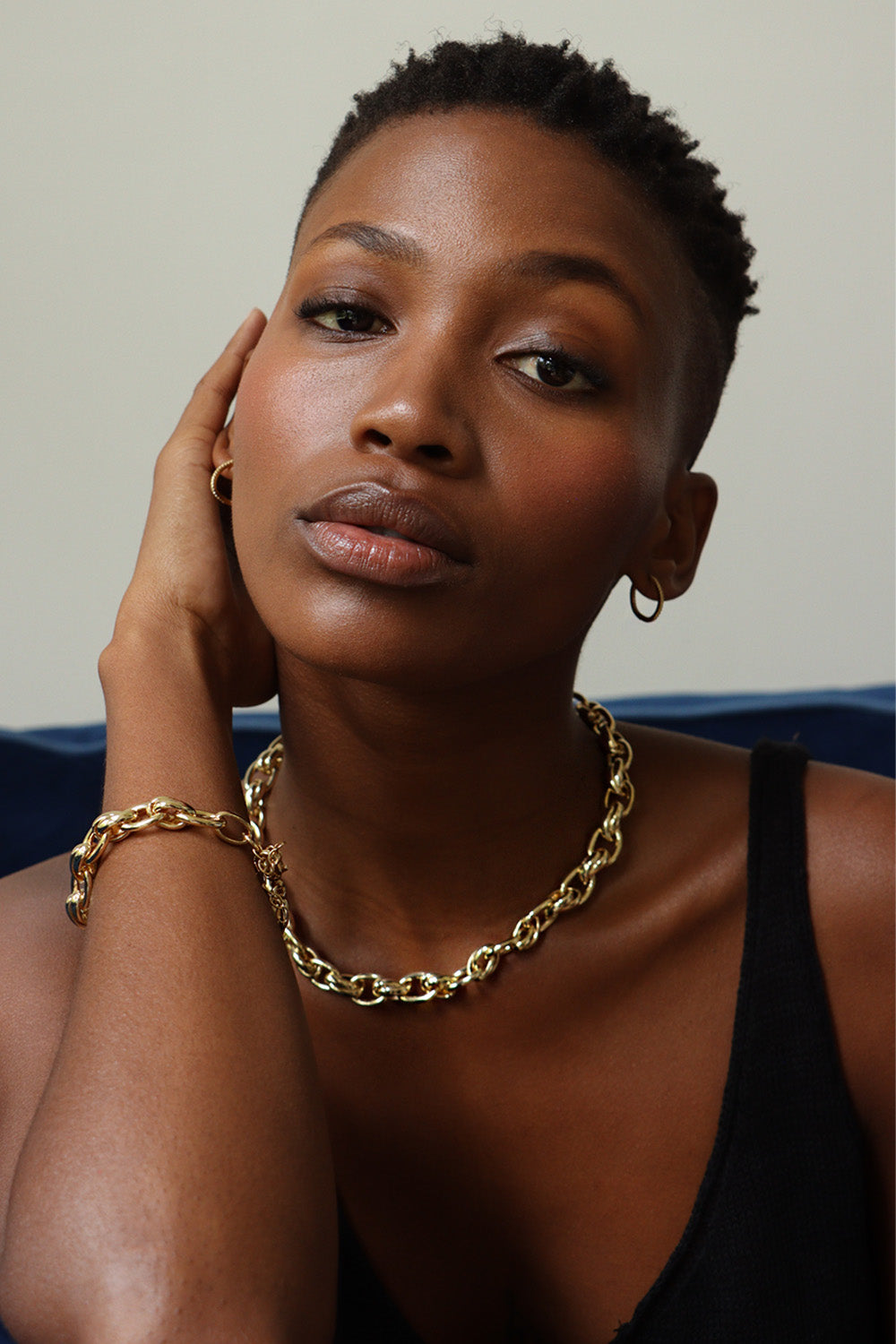 A portrait of a person with short hair wearing gold hoop earrings, a thick gold chain necklace, a matching bracelet, and an Oval Cross Link Necklace.