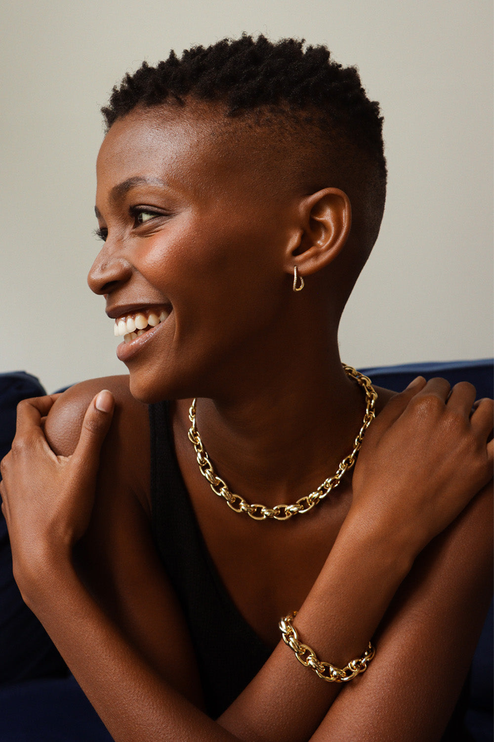 A smiling Black woman with short hair wears a gold Oval Cross Link Necklace and bracelet.