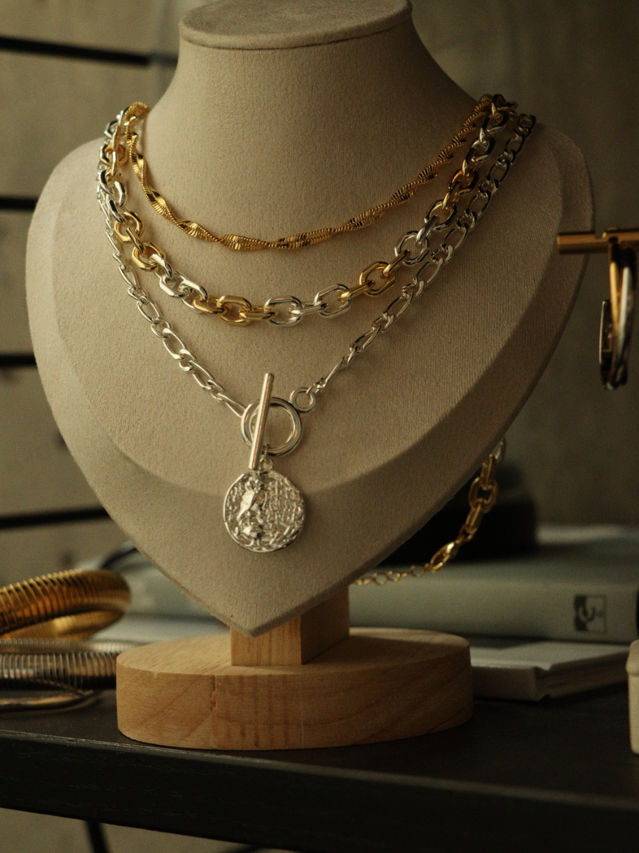 A beige jewelry bust displays layered Athena Silver Toggle Coin necklaces.