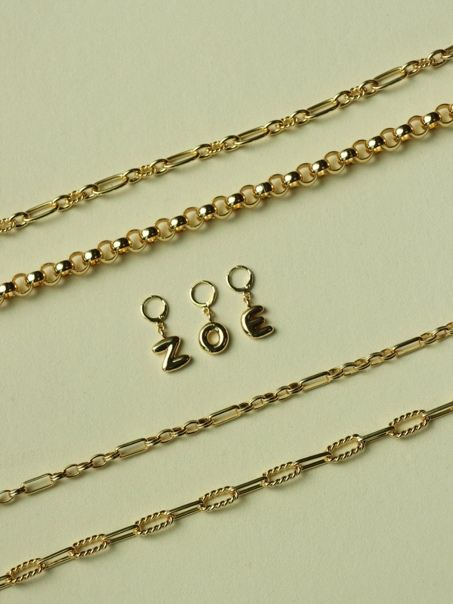 The image shows gold chains and "ZOE" letter charms from Initial Charms.