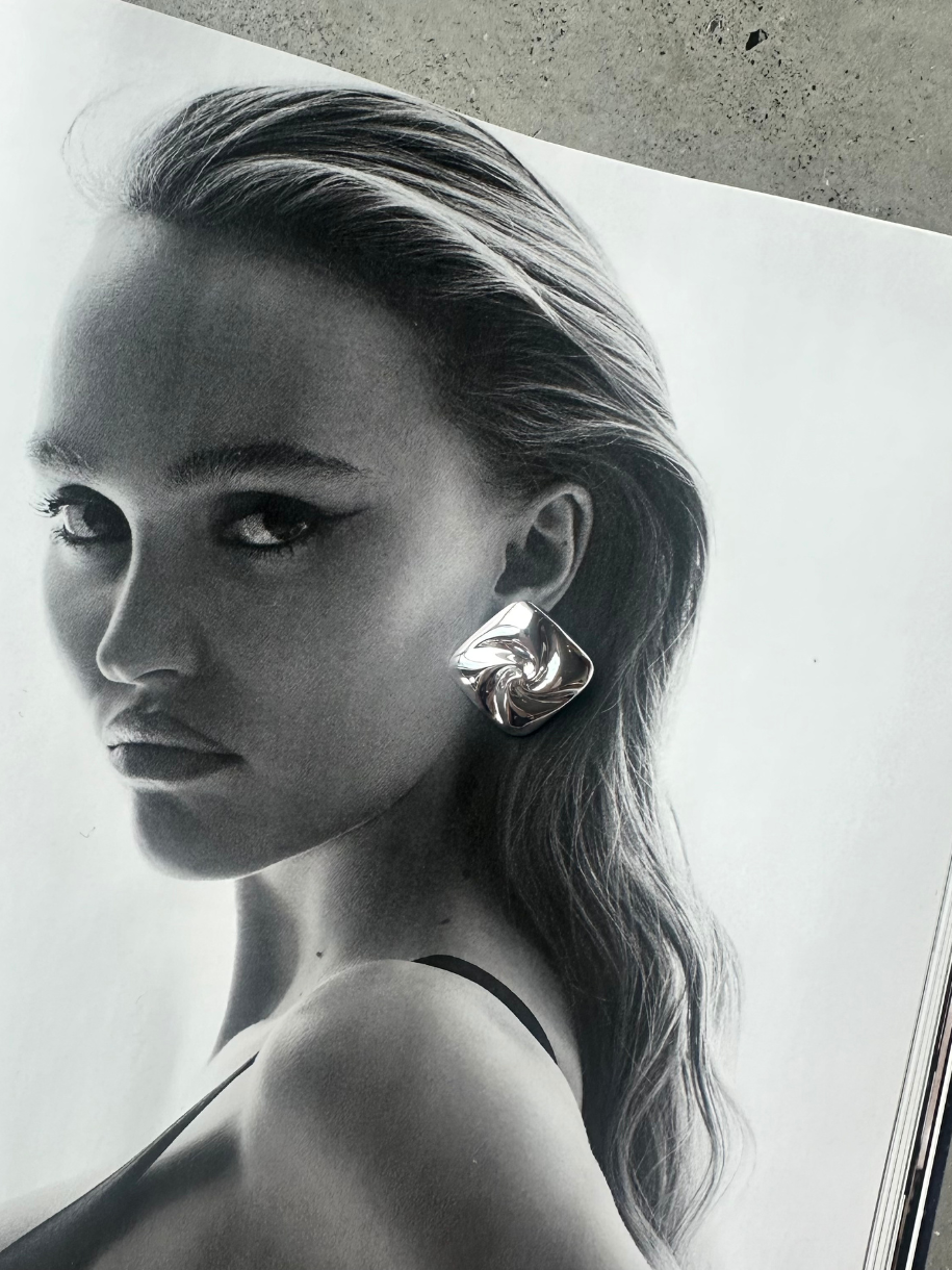 Black and white image of a woman wearing a Bex Square Stud Silver with a swirling design.