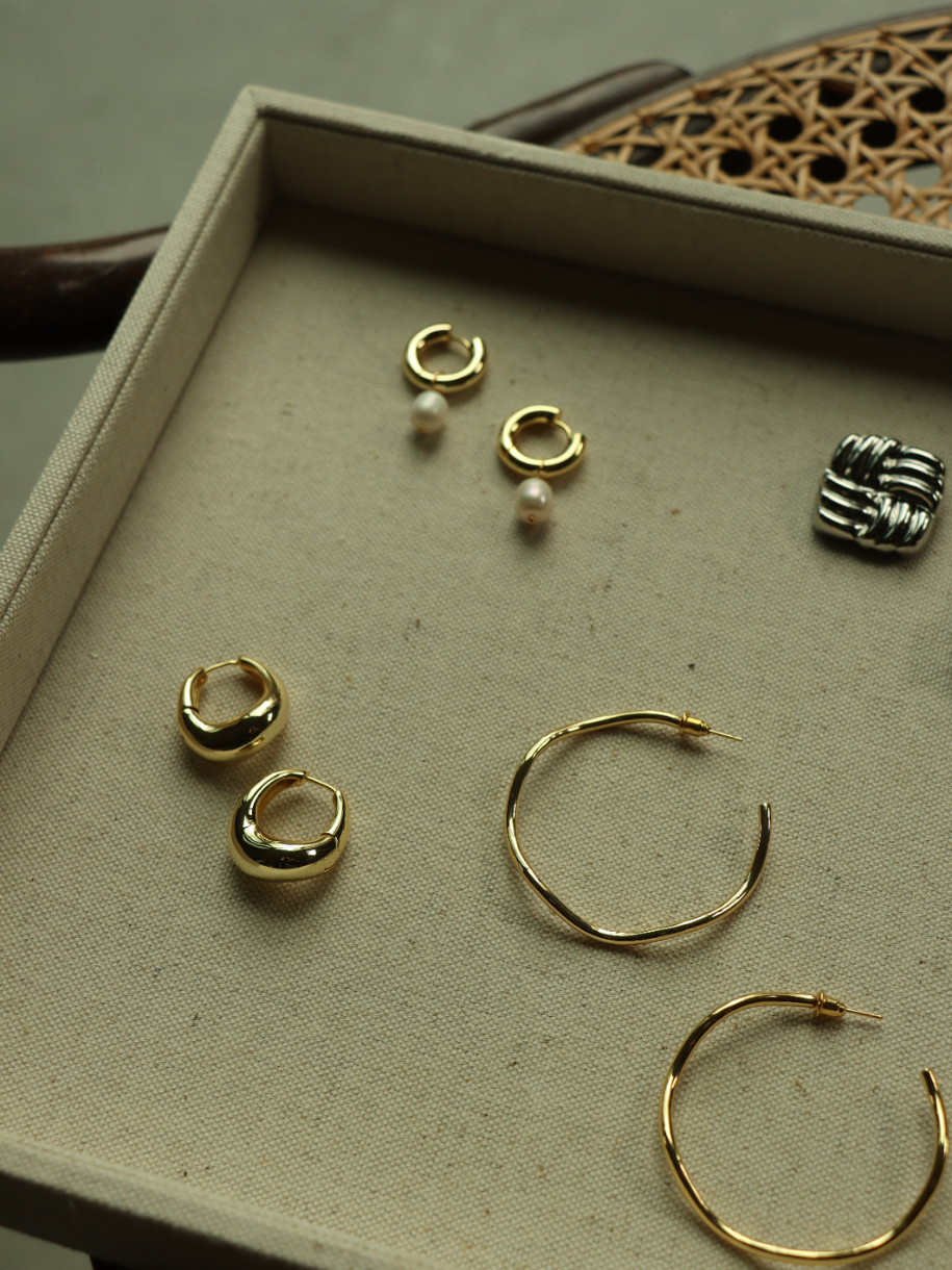 A display tray holds an assortment of gold and silver The Chunky Pearl Hoop earrings.
