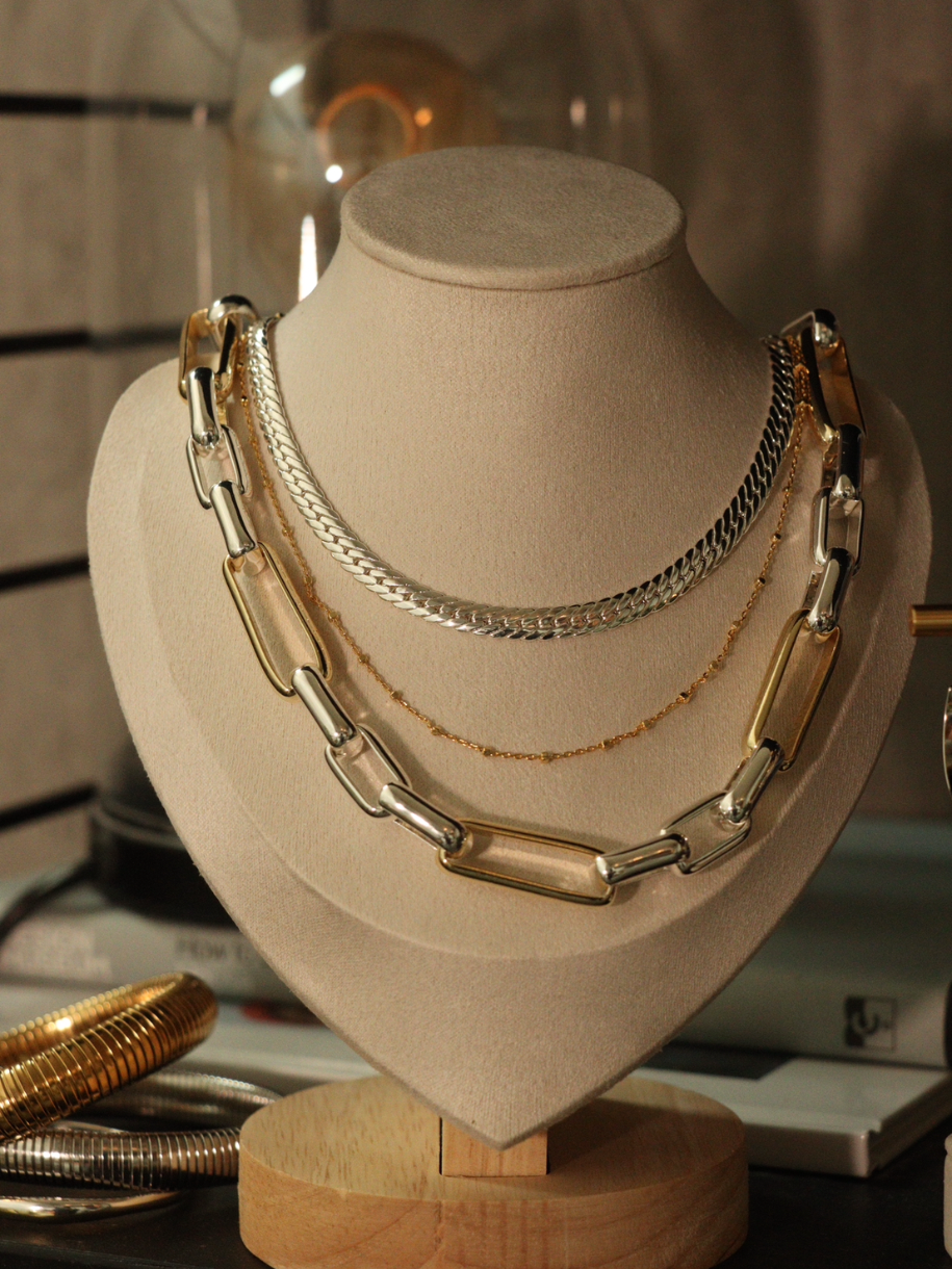 A jewelry display stand presents layered silver Snake Chain and gold-toned necklaces.