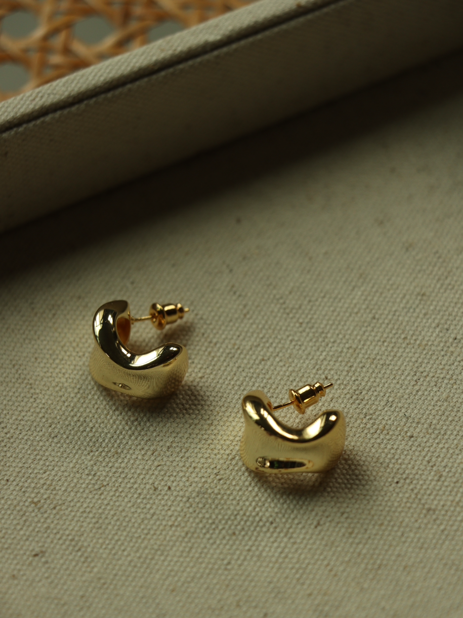 Two gold Opex Hoop earrings rest on a textured surface.