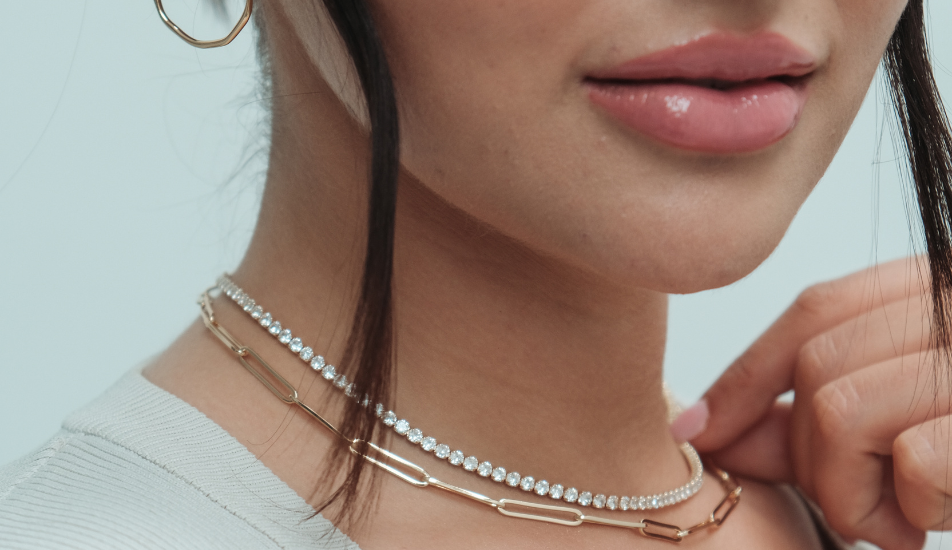 Close-up of a person wearing two necklaces and earrings.