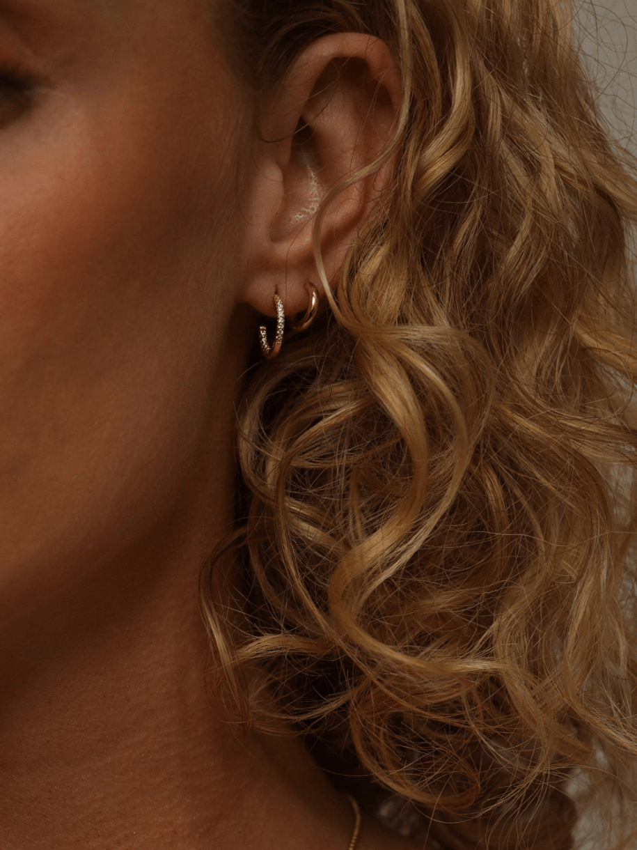 Close-up of a woman's ear with two Plain Gold Huggie Hoop earrings and blonde, curly hair.