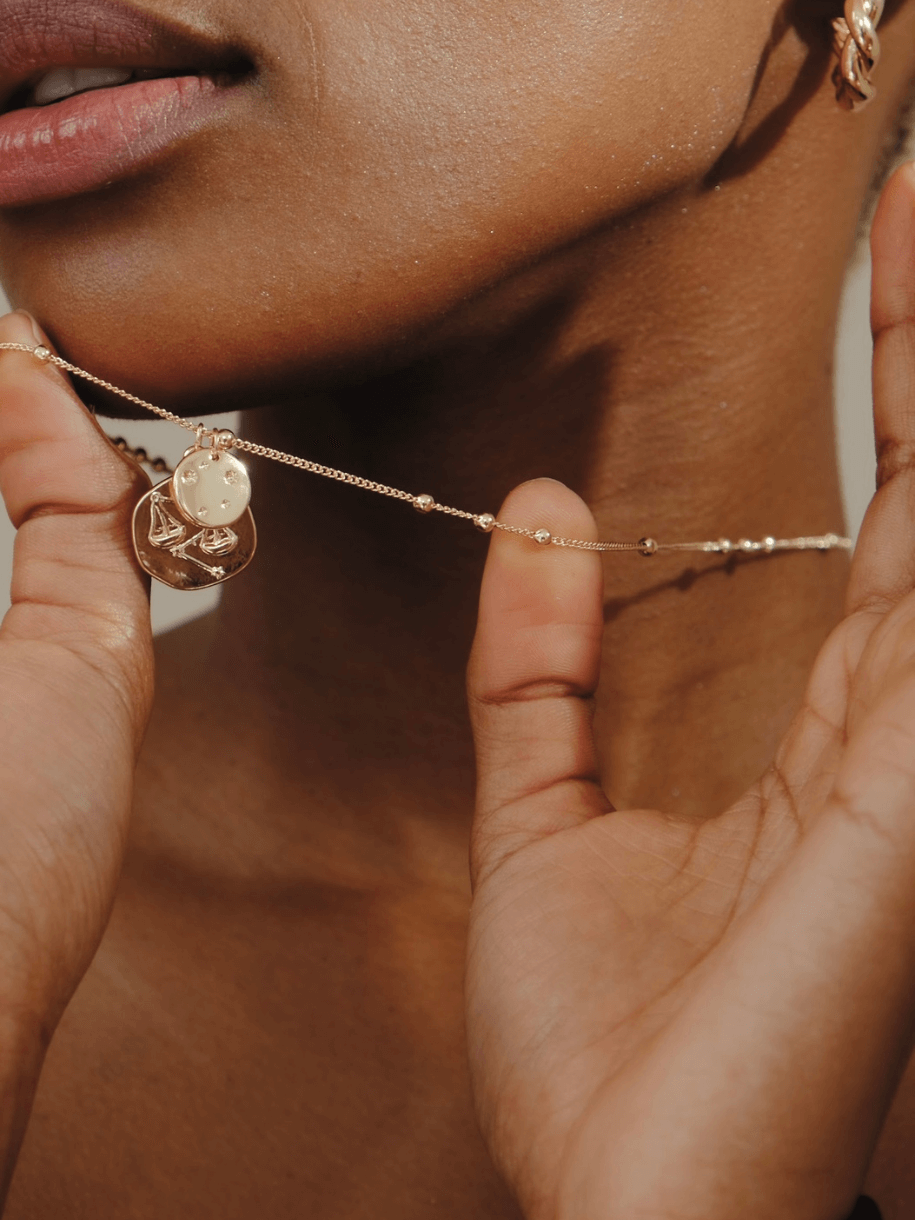 Close-up of a person holding a gold Taurus Zodiac Coin necklace with medallion pendants.