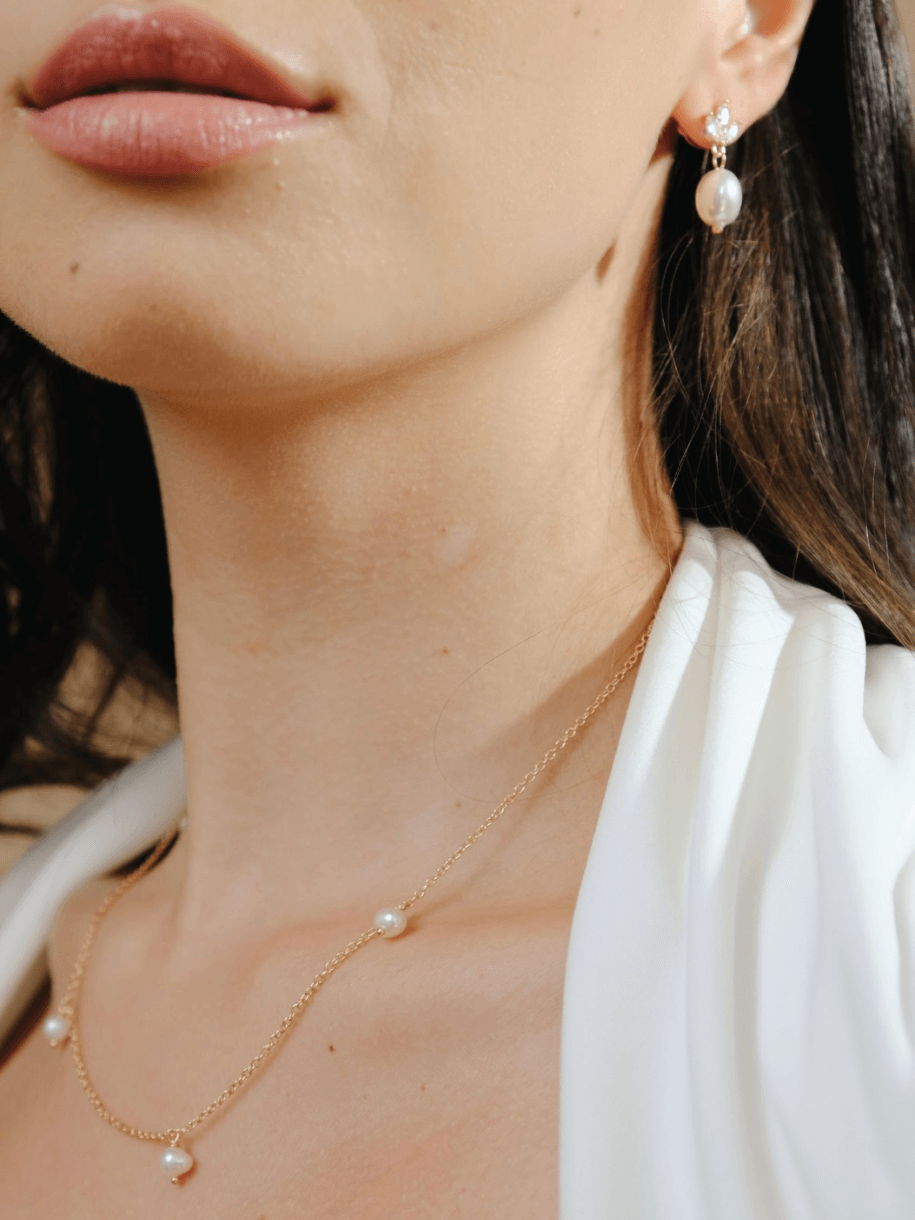 Close-up of a woman's lips, neck, and upper chest, wearing a Bridal Snow Drop Pearl necklace with pearls and pearl earrings.