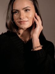 A woman wearing a black sweater and gold Avery Block Necklace touches her face.