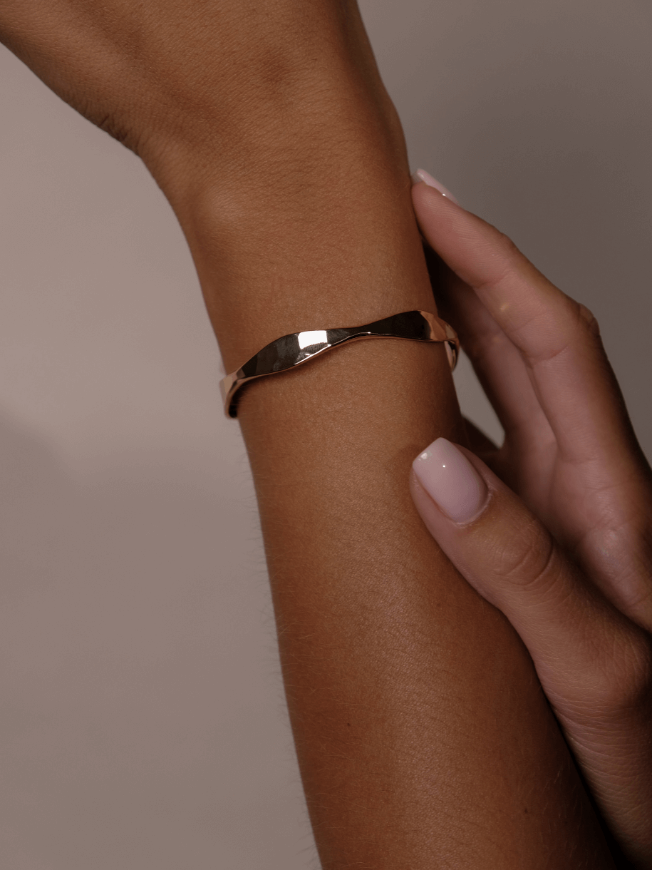 A woman's arm with a twisted gold Block Wave Bangle.