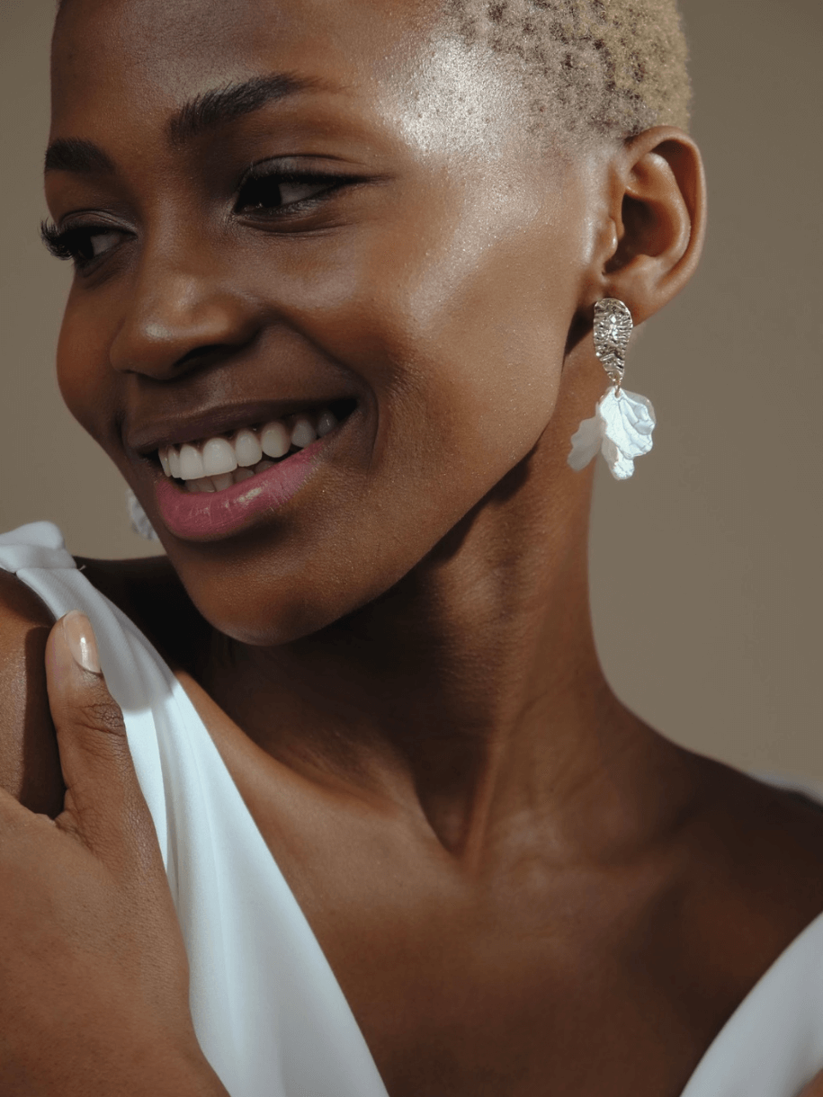 Close-up of a smiling Black woman with short blonde hair, wearing a white garment and Bridal Lumi Earrings.