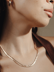Close up of a person's face, neck, and upper chest wearing a gold necklace and gold Chubby Hoop 1.8 hoop earrings.