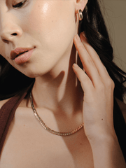 Close-up of a person with a gold chain necklace and Chubby Hoop 1.8 hoop earrings, touching their ear.