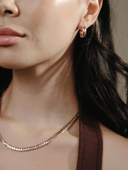 Close-up of a woman wearing Chubby Hoop 1.8 gold hoop earrings and a gold chain necklace.