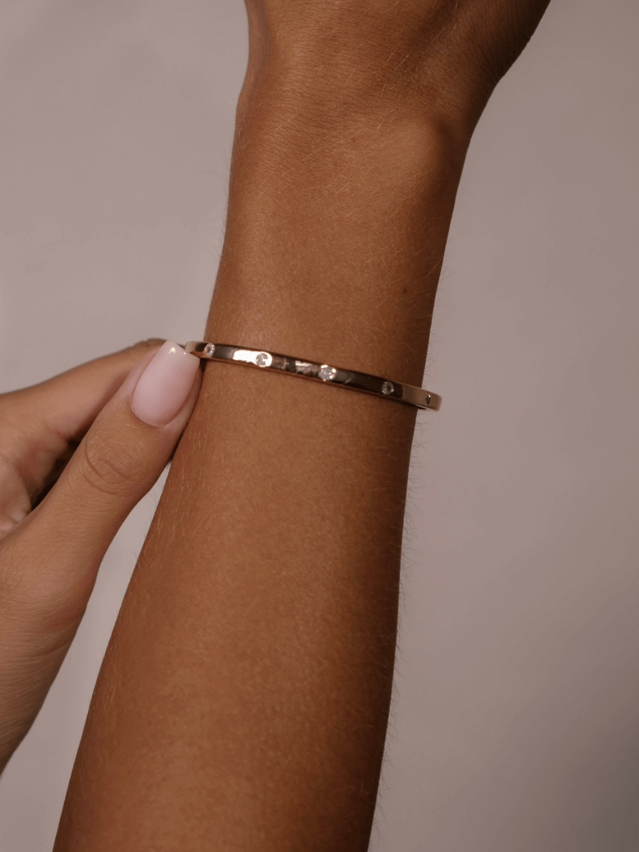 A hand adjusts a Dotted Diamante Bangle with embedded stones on a wrist.