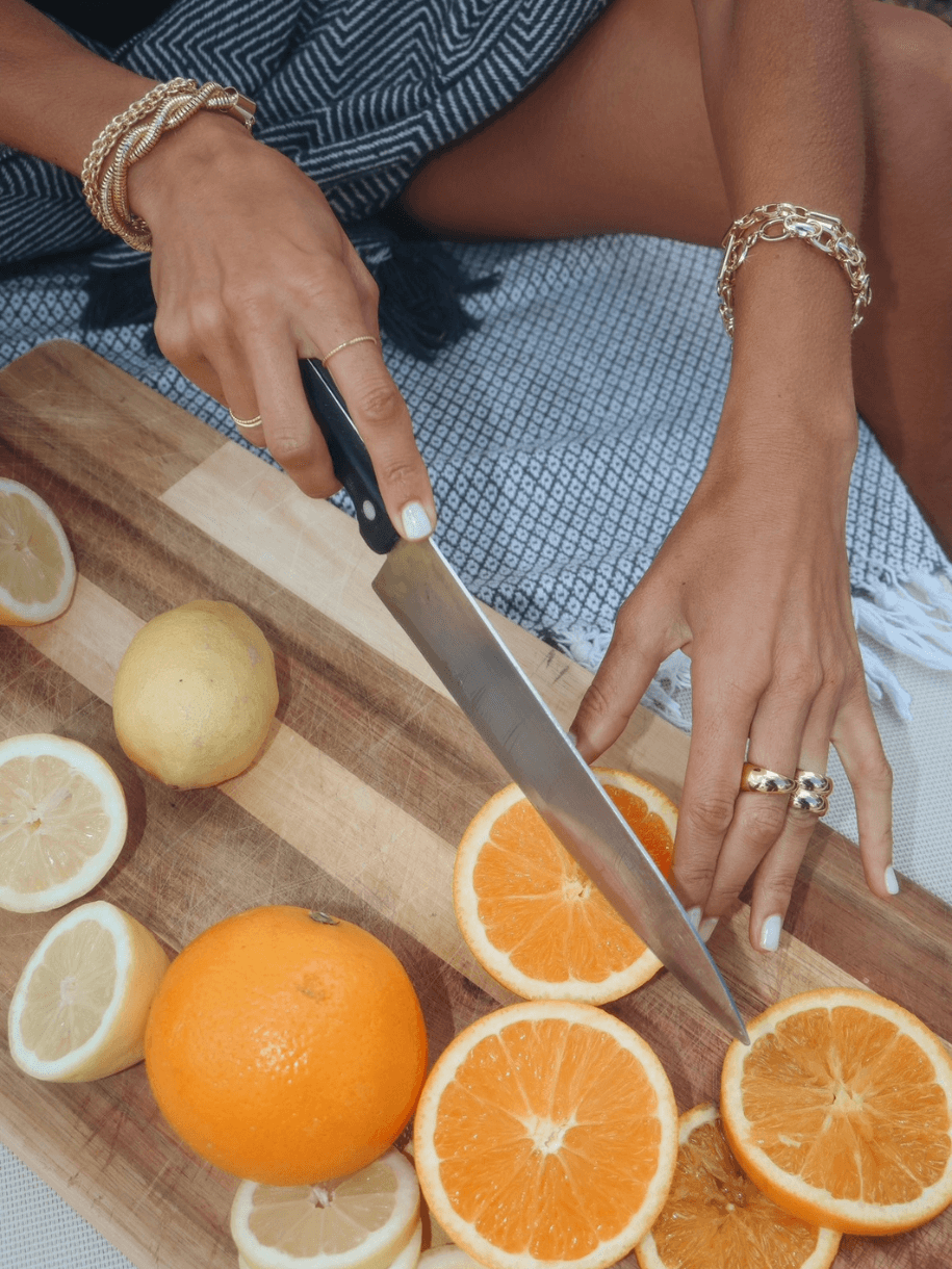 A person wearing a Dome Ring cuts oranges and lemons on a wooden cutting board.