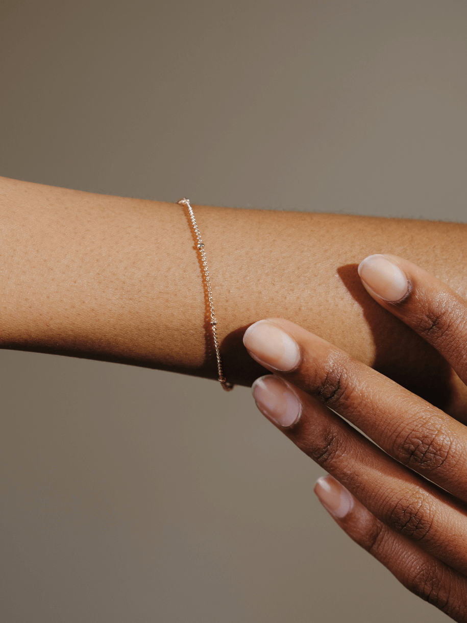 A person's arm wearing a delicate Dotted Gold Bracelet, with their hand nearby.