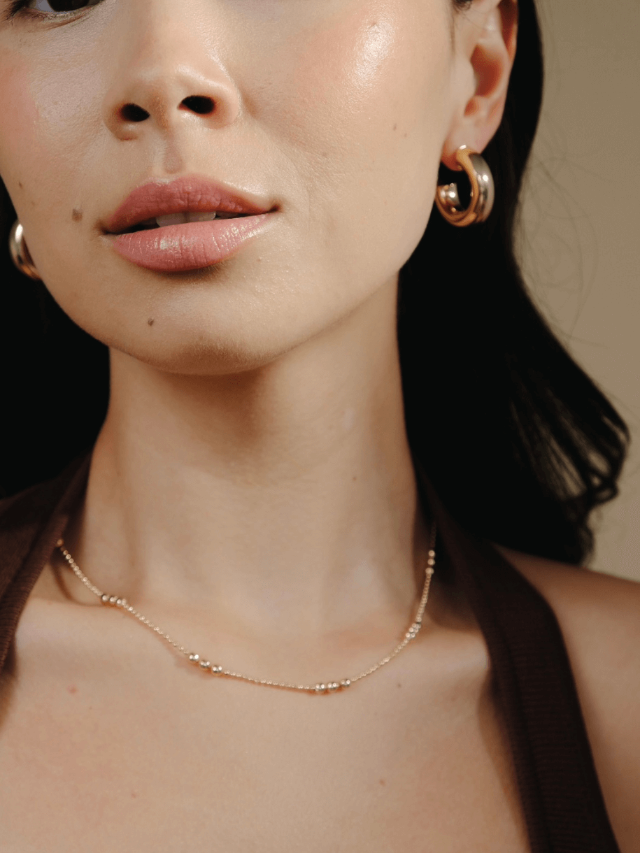 Close-up of a woman wearing gold hoop earrings and The Dotted Ball Necklace 14 inches.