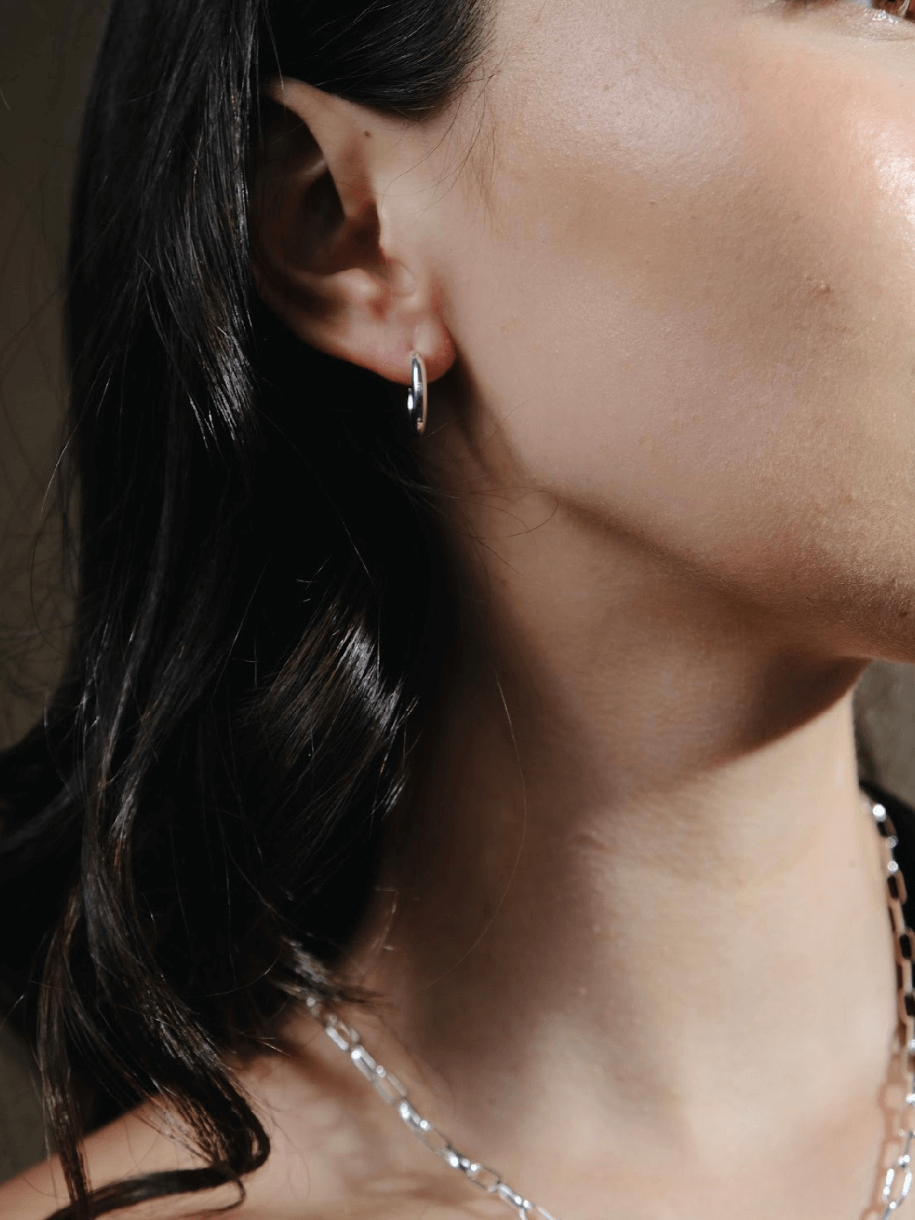 Close-up of a woman's face and upper torso wearing The Iconic Gold Hoop - Extra Small, a black and white striped top, and gold hoop earrings.