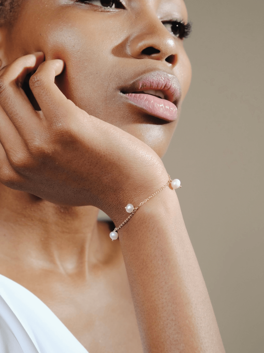 Close-up of a woman with her hand to her face, wearing a Bridal Gr√° Go Deo Pearl Bracelet.